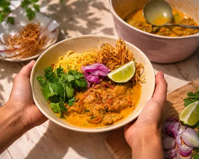 A bowl of khao soi being set down on a sunlit table